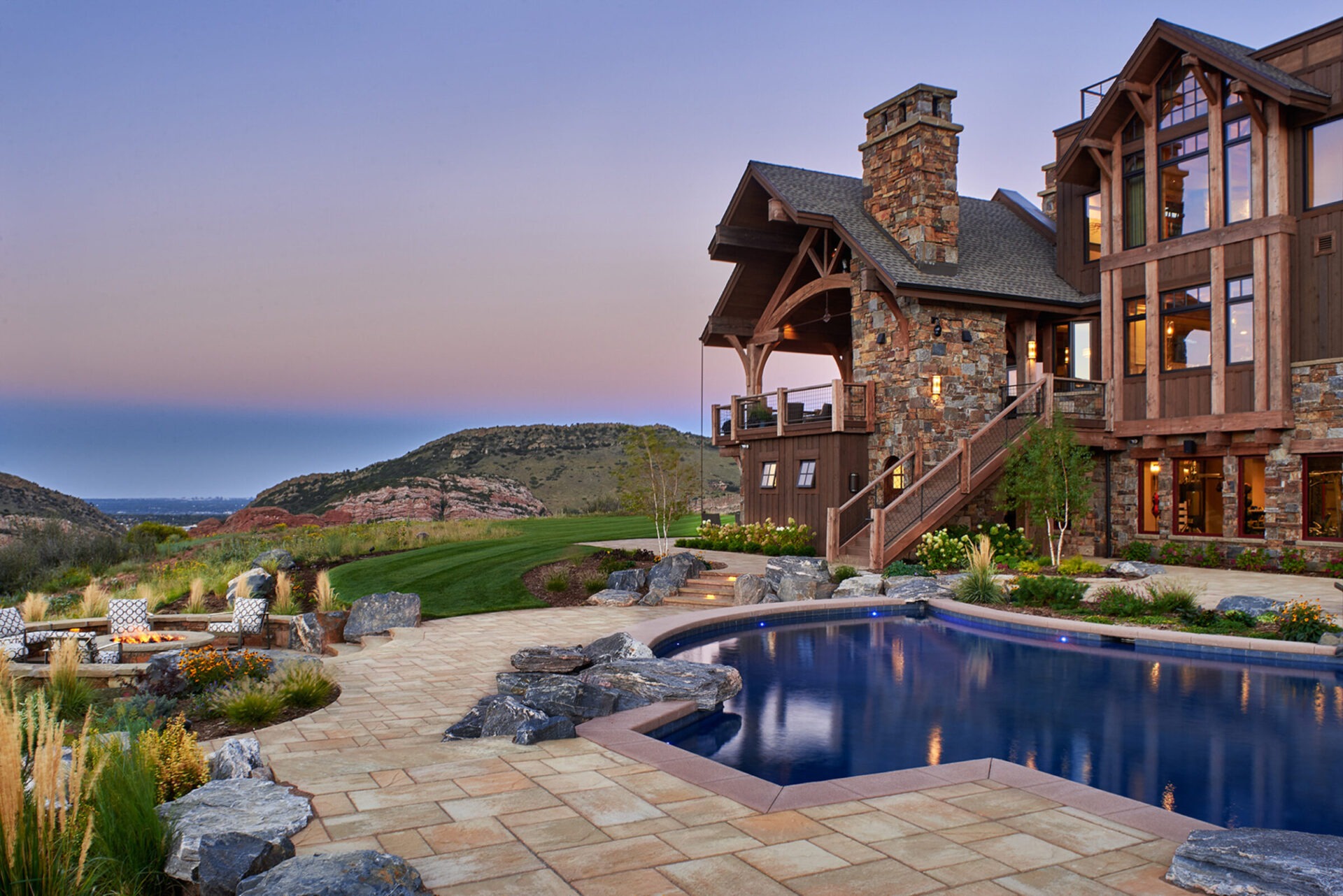 A luxurious stone house with a pool overlooks rolling hills at sunset, featuring a cozy outdoor seating area and lush landscaping.