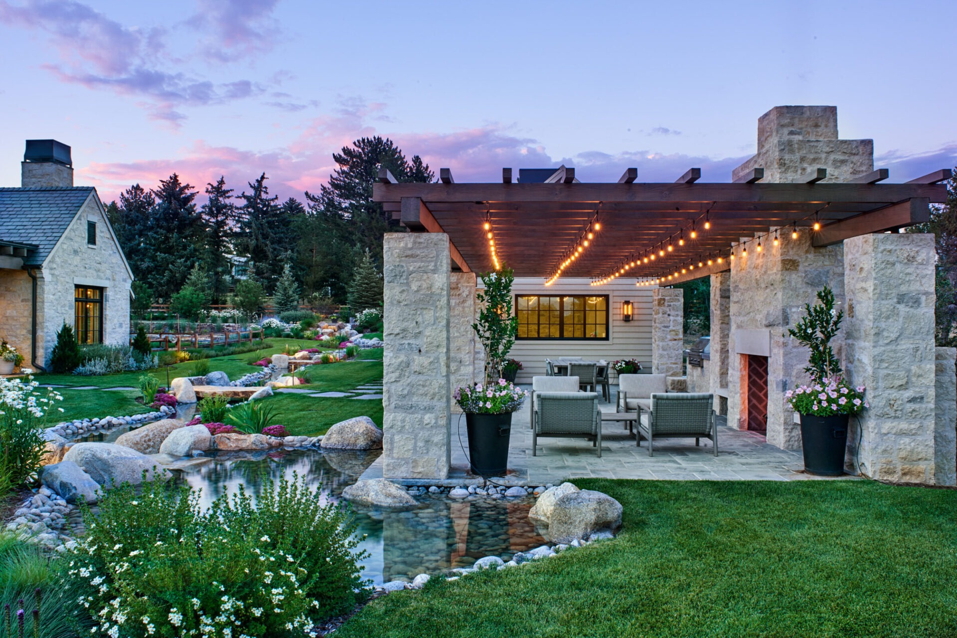 A serene garden scene with a stone pergola, string lights, and a pond surrounded by lush greenery and a cozy house.