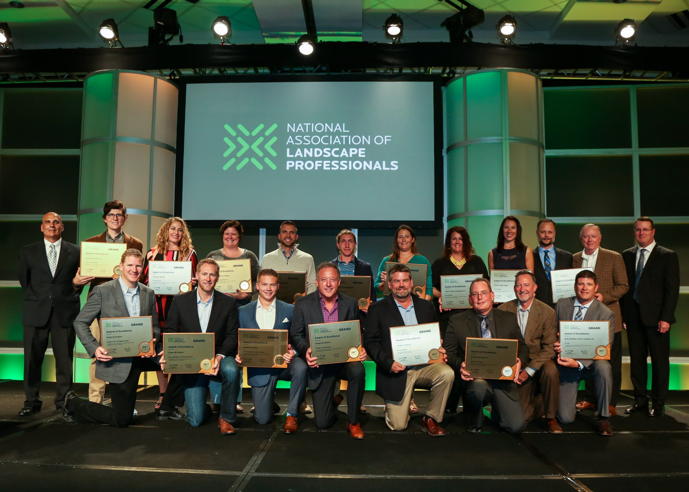 A group of people standing on stage holding awards, with a large sign reading "National Association of Landscape Professionals" in the background.