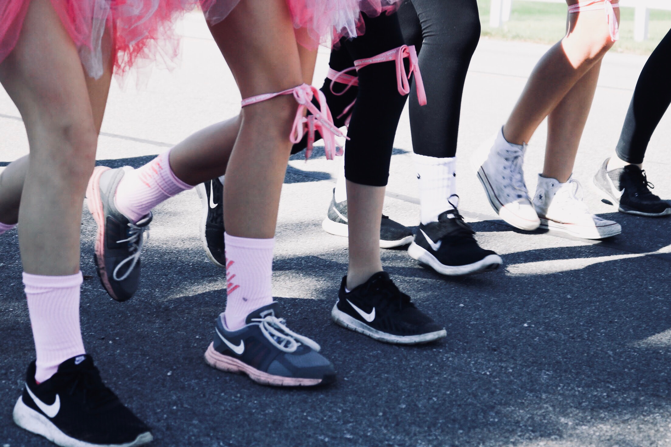 People jogging on a street, wearing pink tutus and athletic shoes, participating in an event, with focus on lower legs and footwear.